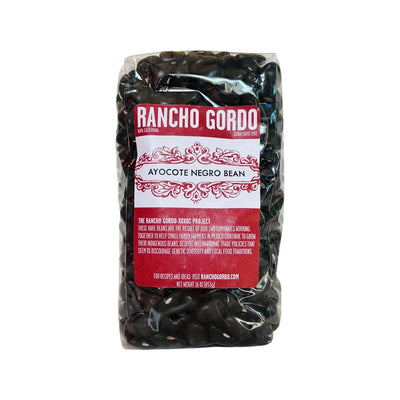 Clear 16 oz single bag of Ayocote Negro (Black) beans with red and white branded label.