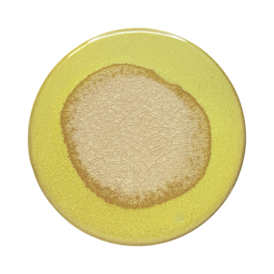 yellow round stoneware trivet with two-tone reactive glaze, showing slight variations in finish.