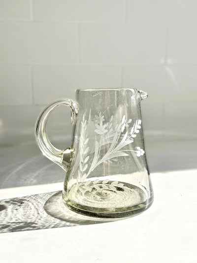 Clear glass pitcher with floral etching on a white surface