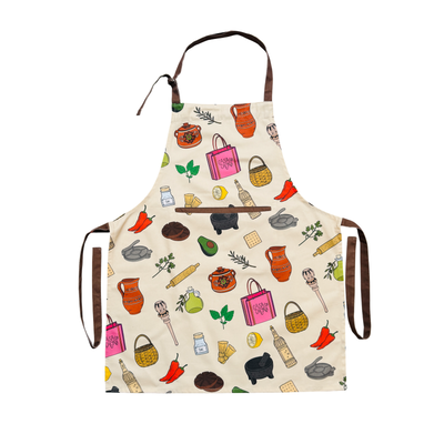 Cream apron with colorful illustrated Mexican kitchen icons—molinillo, molcajete, jarras, chiles, avocado—plus a center pocket, adjustable neck, and brown ties.