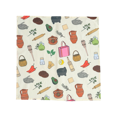 Cream kitchen towel covered in illustrated Mexican-kitchen motifs including a black molcajete with pestle, wooden molinillo, avocado half, lemon slice, rosemary sprig, terracotta pot, rolling pin, cracker, and oil bottle.