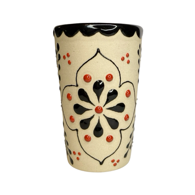 cream ceramic shot glass decorated with colorful floral designs in red, black, and orange.