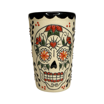 cream ceramic shot glass decorated with colorful sugar skull (Catrina) designs in red, black, and orange.