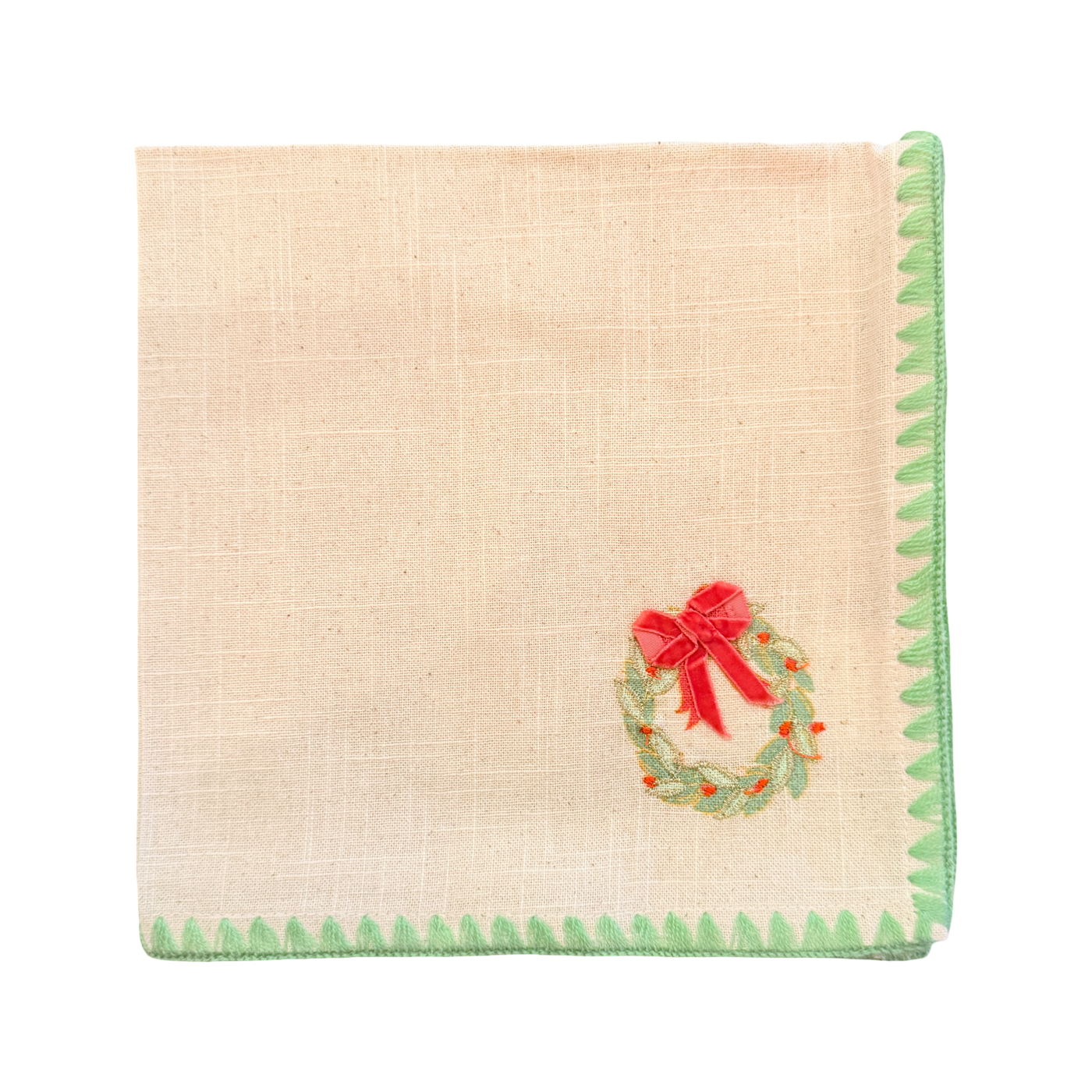 Beige napkin with green trim and a red bow and wreath design