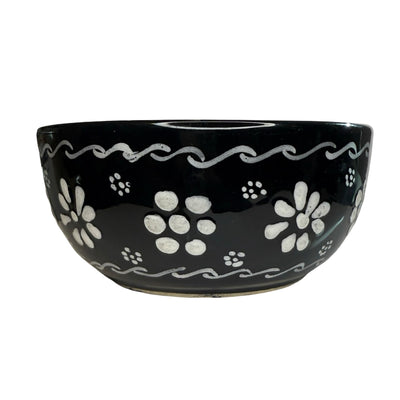 black ceramic bowl hand-painted with white floral and scrollwork designs.