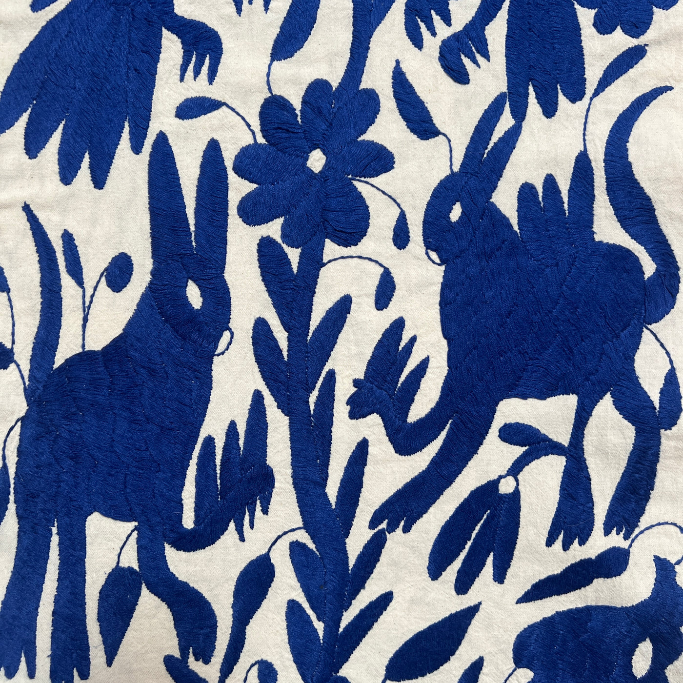 enhanced view of royal blue floral and fauna scenery detail embroidered on off white table runner