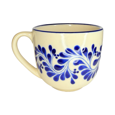 cream ceramic mug decorated with hand-painted blue floral vine patterns and rounded handles.