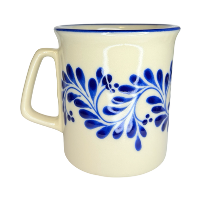 cream ceramic tarro mug with hand-painted blue floral vine patterns and squared handles.