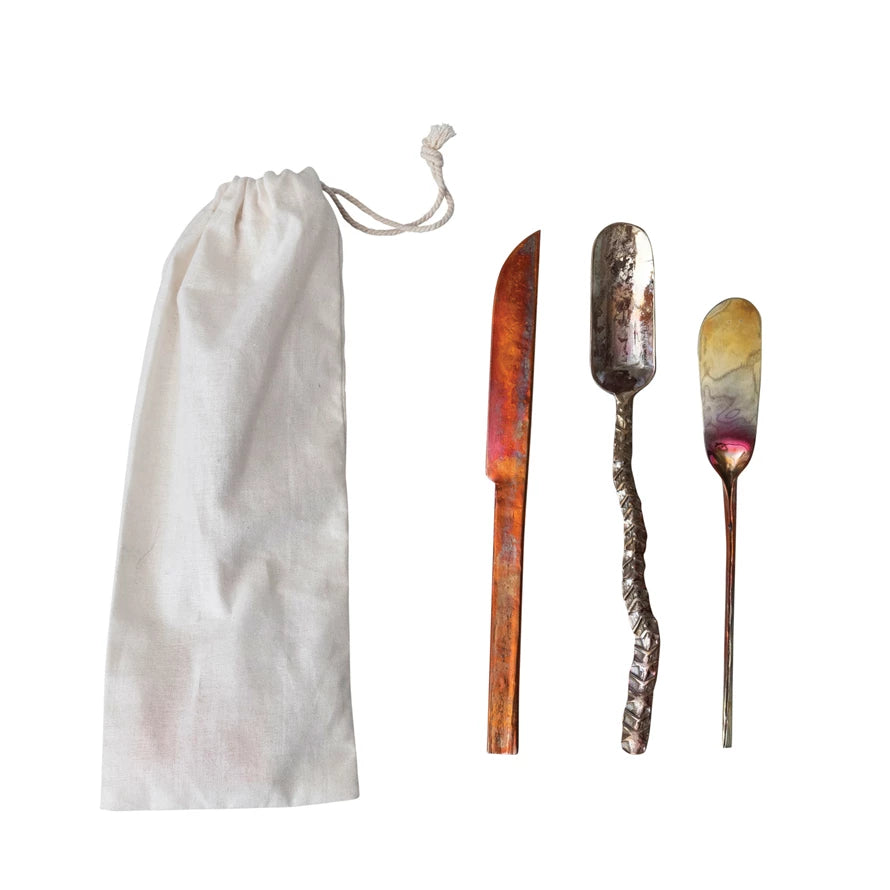 Set of three hand-forged copper canapé knives in assorted shapes and finishes, shown with a white cotton drawstring storage bag.