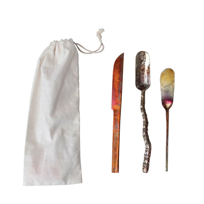 Set of three hand-forged copper canapé knives in assorted shapes and finishes, shown with a white cotton drawstring storage bag.