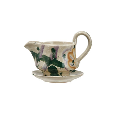 Hand-painted ceramic creamer with saucer featuring green, purple, and yellow brushstroke patterns on a cream background.