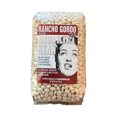 16 oz clear bag of Alubia Blanca (white) beans with a white and maroon branded label that features an image of a woman licking her lips.