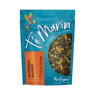 A teal resealable bag of Té Marín Moringa Mango Tea with a clear window showing the loose herbal blend inside. The packaging features a colorful hummingbird and text in English and Spanish.