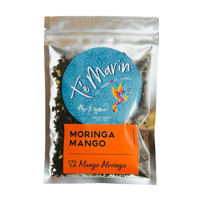 A clear resealable bag of loose leaf tea labeled “Te Marin.” The packaging features a blue circular logo with a colorful hummingbird and an orange label that reads “Moringa Mango” and “Te Mango Moringa.”