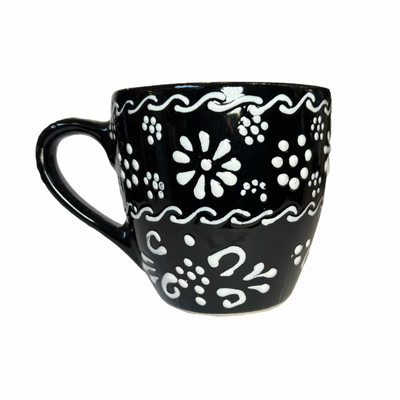 black mug with a white design featuring flowers and filagree