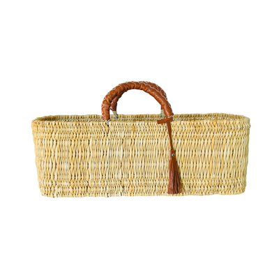 A rectangular woven reed market basket with sturdy leather-wrapped handles and tassel.