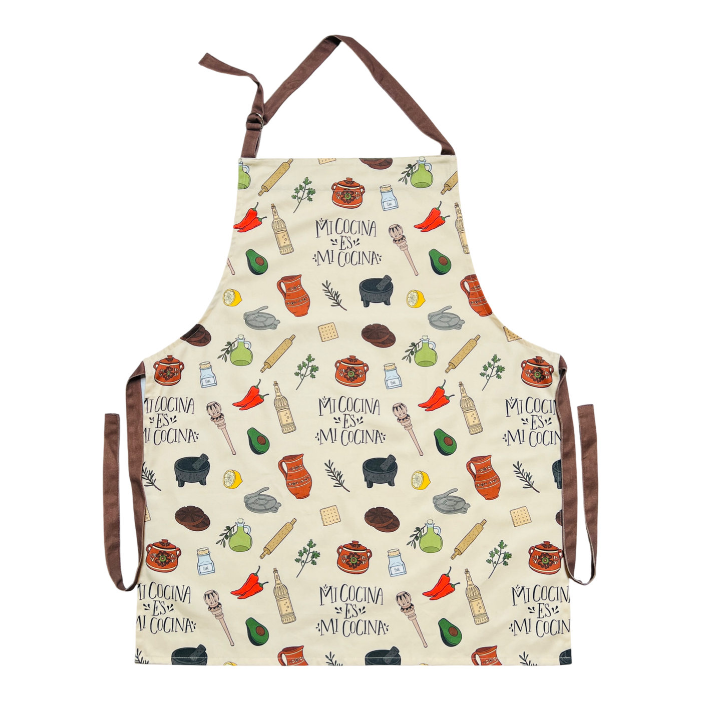 cream apron with images of various Mexican kitchen essentials such as a molcajete and olla as well as the phrase Mi Cocina Es Mi Cocina featuring brown waist ties and neck loop.