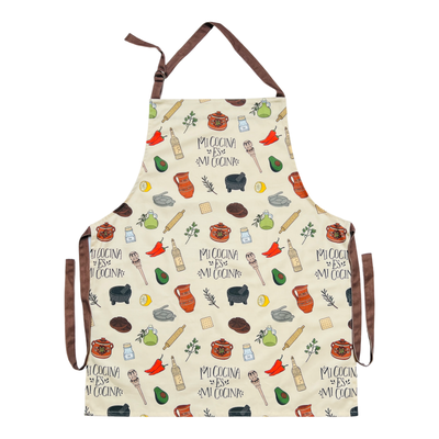 cream apron with images of various Mexican kitchen essentials such as a molcajete and olla as well as the phrase Mi Cocina Es Mi Cocina featuring brown waist ties and neck loop.