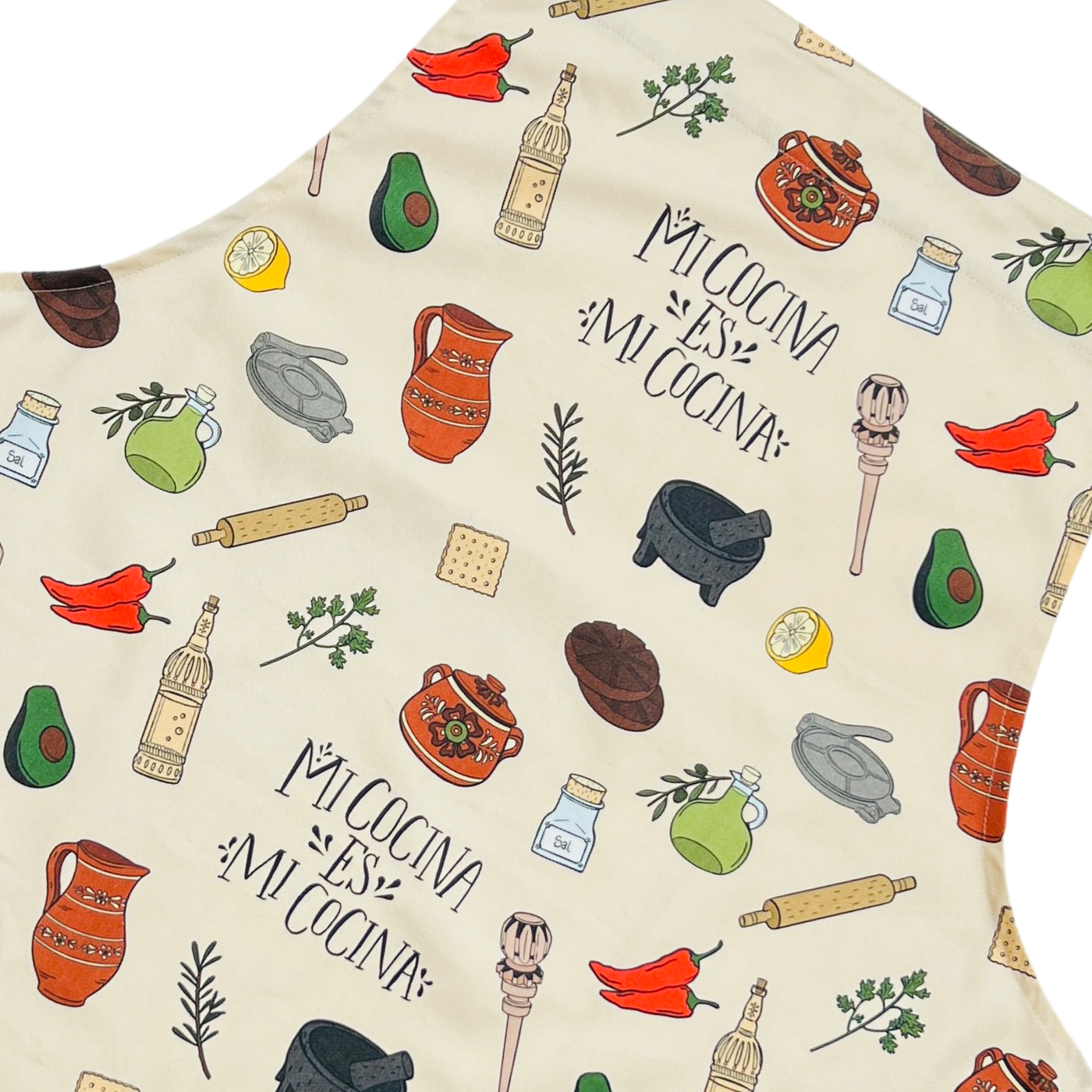 close up view of a cream apron with images of various Mexican kitchen essentials such as a molcajete and olla as well as the phrase Mi Cocina Es Mi Cocina