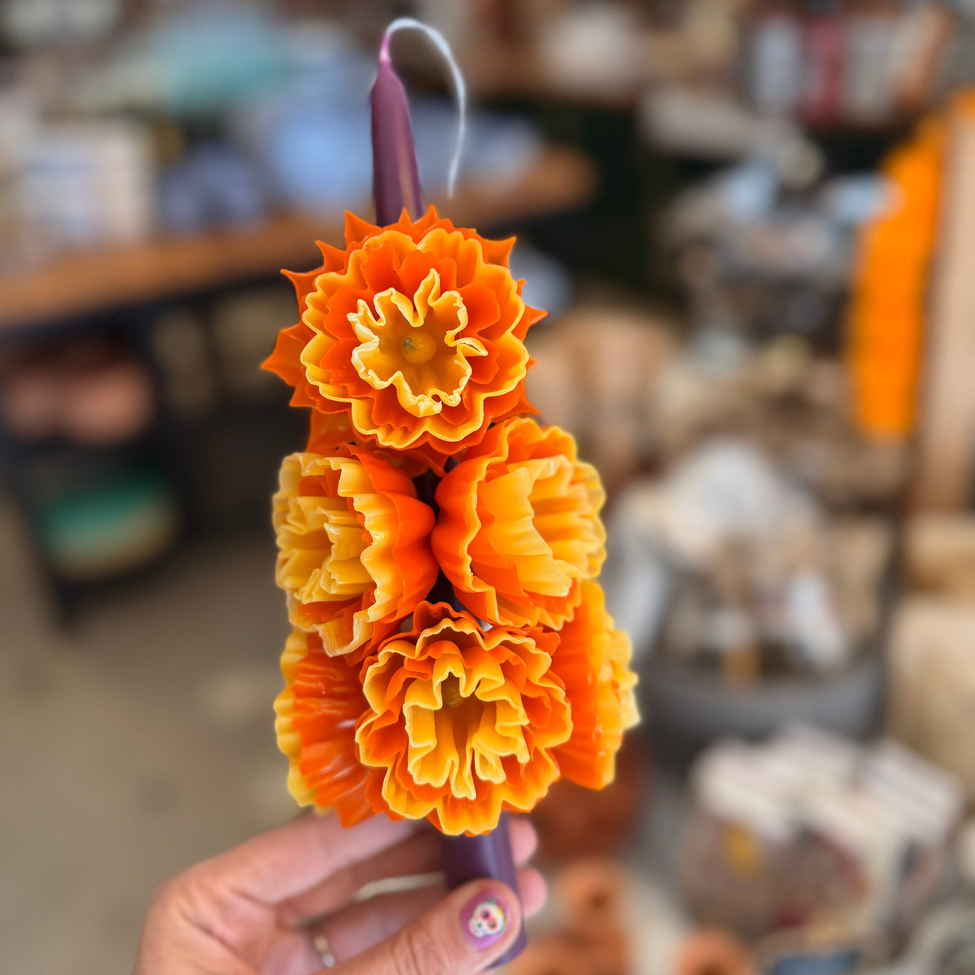 alternate photo of purple stick candle decorated with multiple wax marigolds 