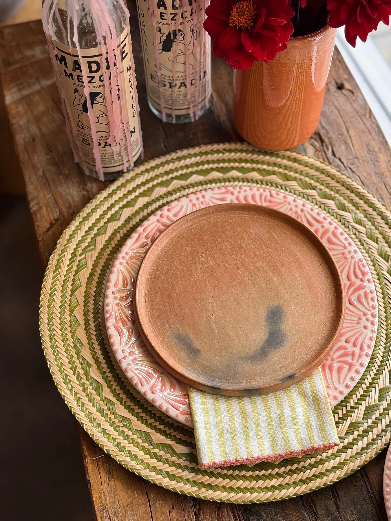 Green and natural round placemat topped with multicolored dinner and salad plate and striped napkin all on a wooden tabletop.