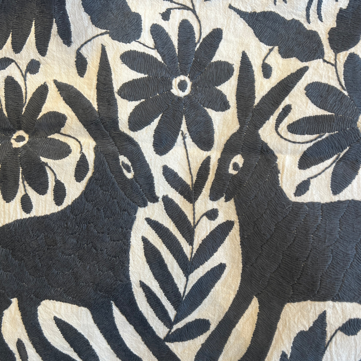 enhanced view of dark gray floral and fauna scenery detail embroidered on off white table runner