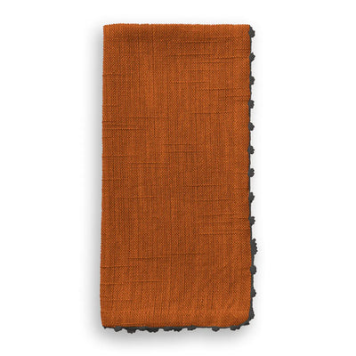 Folded cotton napkin in a warm tomato cream color with grey knotted trim detail.