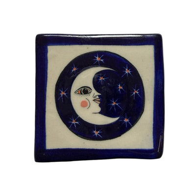 square ceramic coaster with a blue border with a blue circle in the center that features a crescent moon with a face surrounded by stars.
