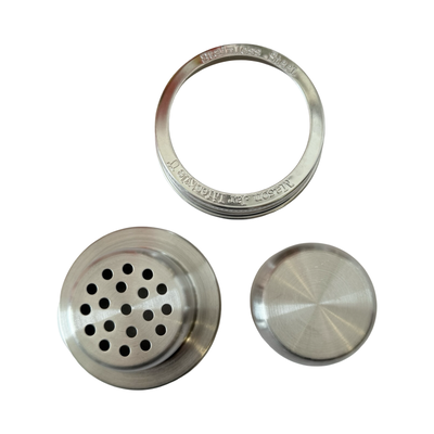 Close-up of a stainless steel mason jar cocktail shaker lid set, including a strainer insert, cap, and screw band marked with "Stainless Steel" engraving.