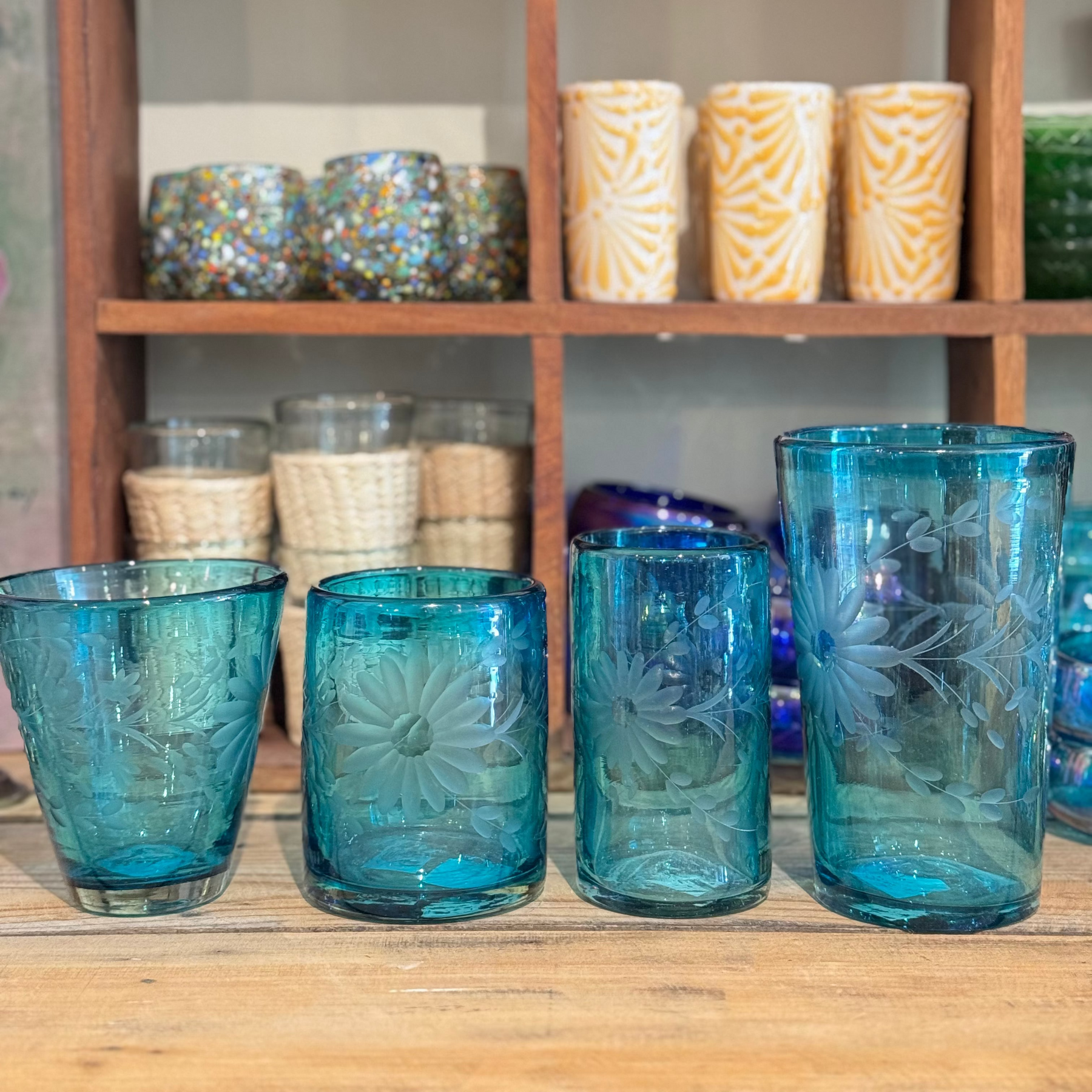 Blue glass tumblers on a wooden surface with shelves of decorative items in the background.