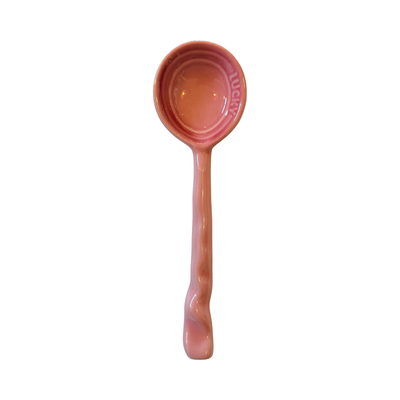 A pink ceramic spoon with a glossy finish and a curved handle design.