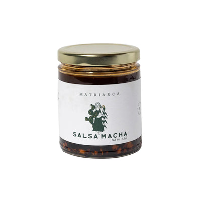 7. oz Glass jar labeled “Salsa Macha” by Matriarca, filled with dark red chile oil and visible pistachio and chile pieces, with a gold lid.