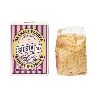 A box and clear bag of Siesta Co. Smoked Ginger Mediterranean Sea Salt Flakes, featuring delicate golden flakes of infused sea salt.