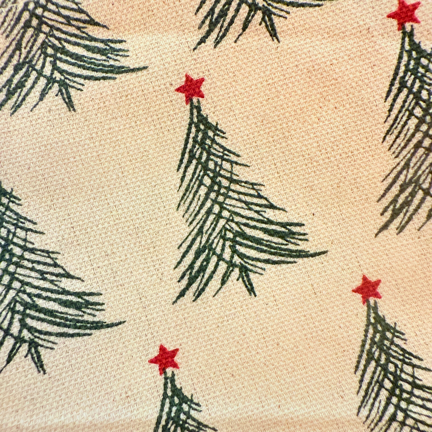 close up view of a stonewashed cotton napkin printed with green Christmas trees topped with red stars.
