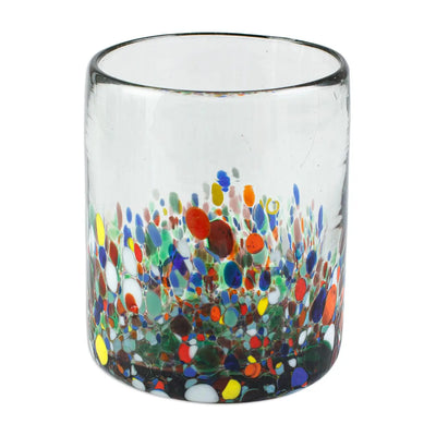 Clear handblown glass juice glass decorated with multicolored floral-like confetti patterns in red, yellow, blue, green, and white near the base.