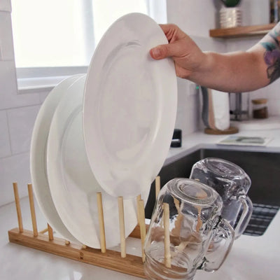 bamboo drying rack on a counter with white plates and two mason jars featuring an individual adding a white plate to the rack.