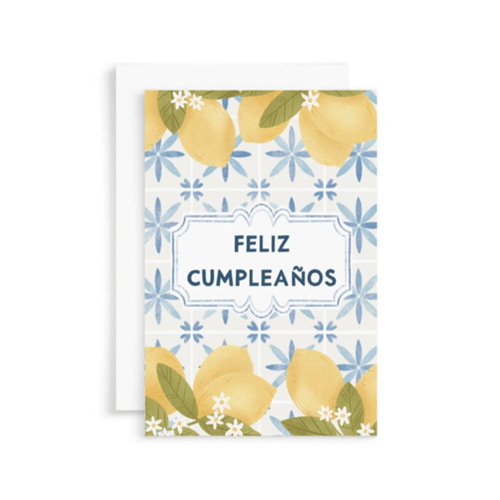 white card with illustrations of lemons and lemon blossoms, blue floral background and the phrase feliz cumpleanos in dark blue lettering.