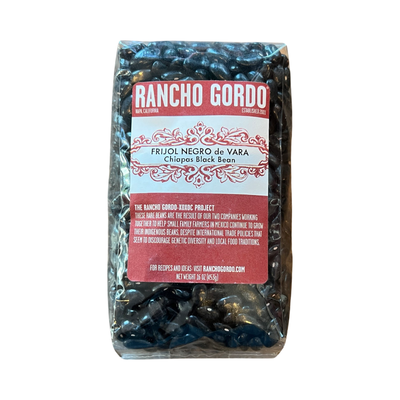 16 oz clear bag of Chiapas Black Bean with a white and maroon branded label featuring an image of a woman licking her lips.