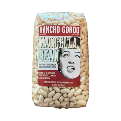 16 oz clear bag of white Marcella beans with a white and maroon branded label featuring an image of a woman licking her lips.