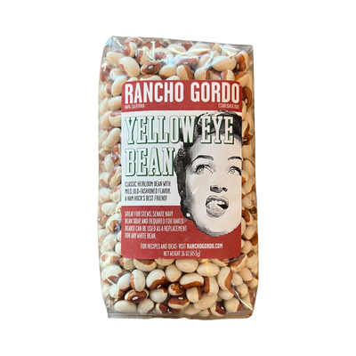 16 oz clear bag of yellow eye bean with a white and maroon branded label featuring an image of a woman licking her lips.