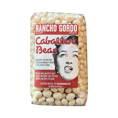 16 oz clear bag of white caballero bean with a white and maroon branded label featuring an image of a woman licking her lips.