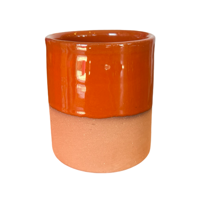 A handcrafted terracotta cup with a rust-colored glazed upper half and an unglazed earthy terracotta base.