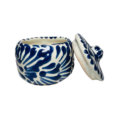 Side view of a ceramic container with a blue and white Puebla design and the lid leaning on the side of it.
