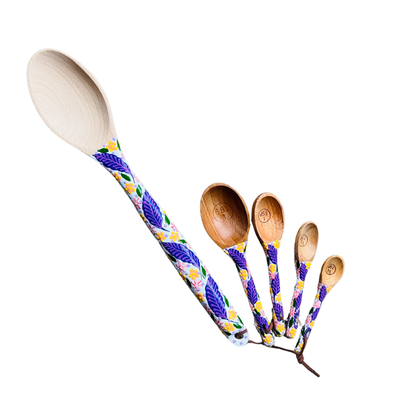 A baking spoon and a set of 4 measuring wooden spoons with white handles and a purple and yellow floral design.