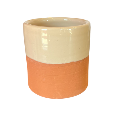 A handcrafted terracotta cup with a cream-colored glazed upper half and an unglazed earthy terracotta base.