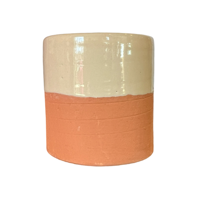 A handcrafted terracotta cup with a cream-colored glazed upper half and an unglazed earthy terracotta base.