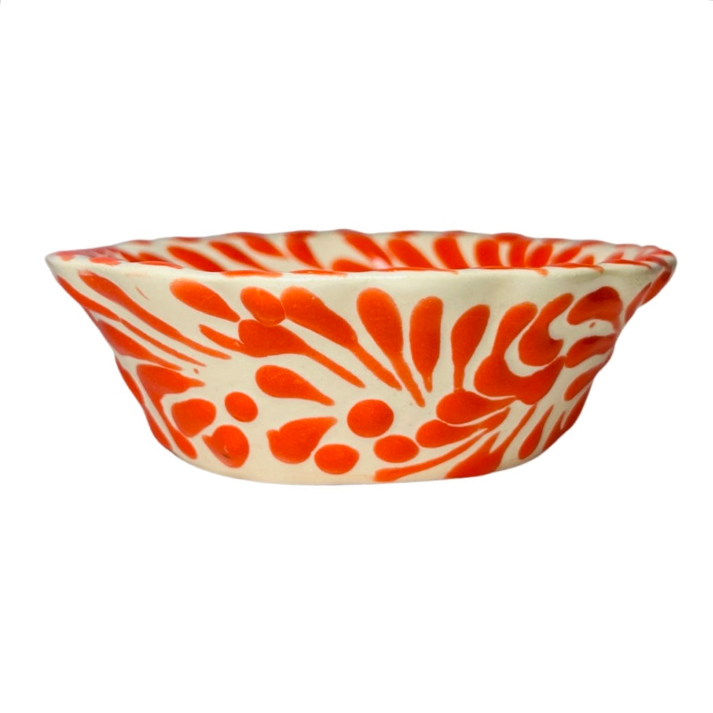 side view of a orange and white Puebla design ceramic bowl with a scalloped edge