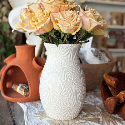 White textured vase with flowers on a table with decorative items