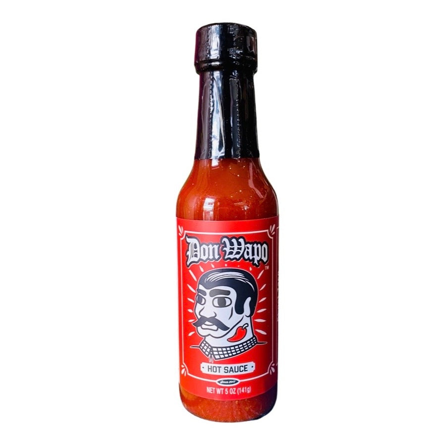 Front view of a glass bottle containing 5 oz of hot sauce. The label is red features a graphic of a man with slicked back black hair, giant black eyebrows, a black mustache, and a red chili pepper tattoo on his neck. 