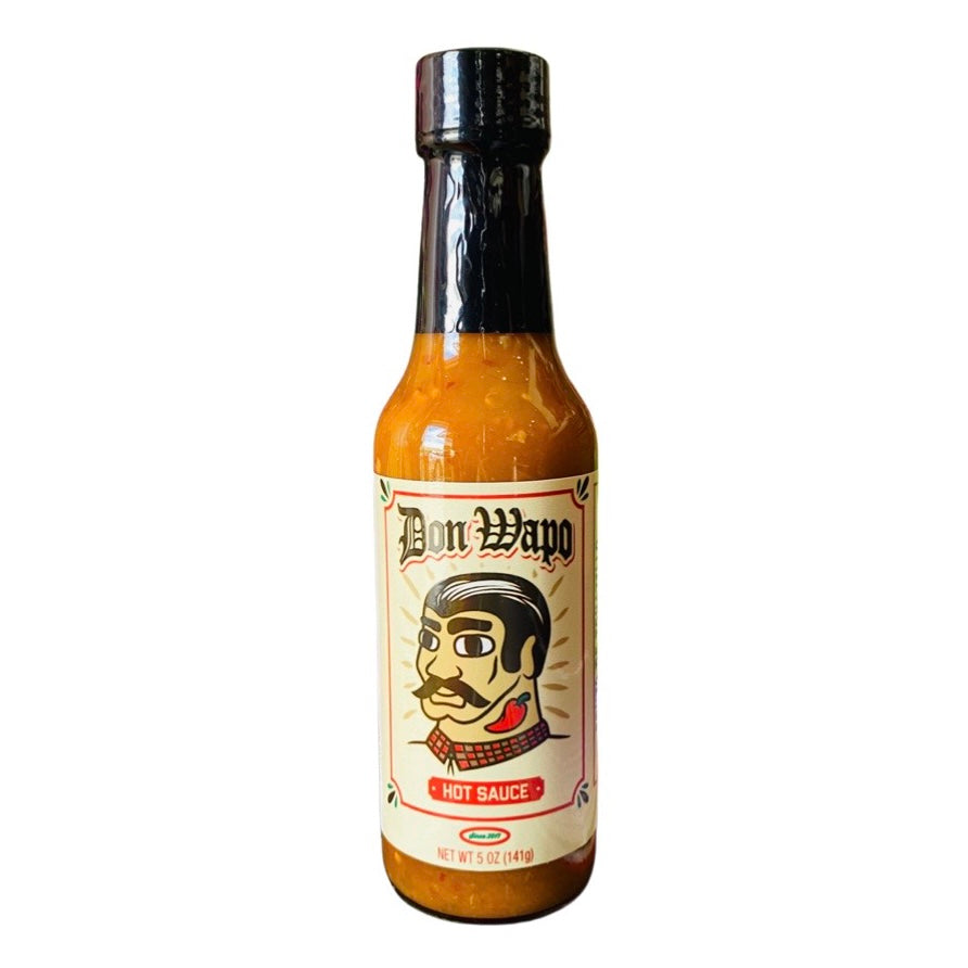 Front view of a glass bottle containing 5 oz of hot sauce. The label is a cream color featuring a graphic of a man with slicked back black hair, giant black eyebrows, a black mustache, and a red chili pepper tattoo on his neck. 
